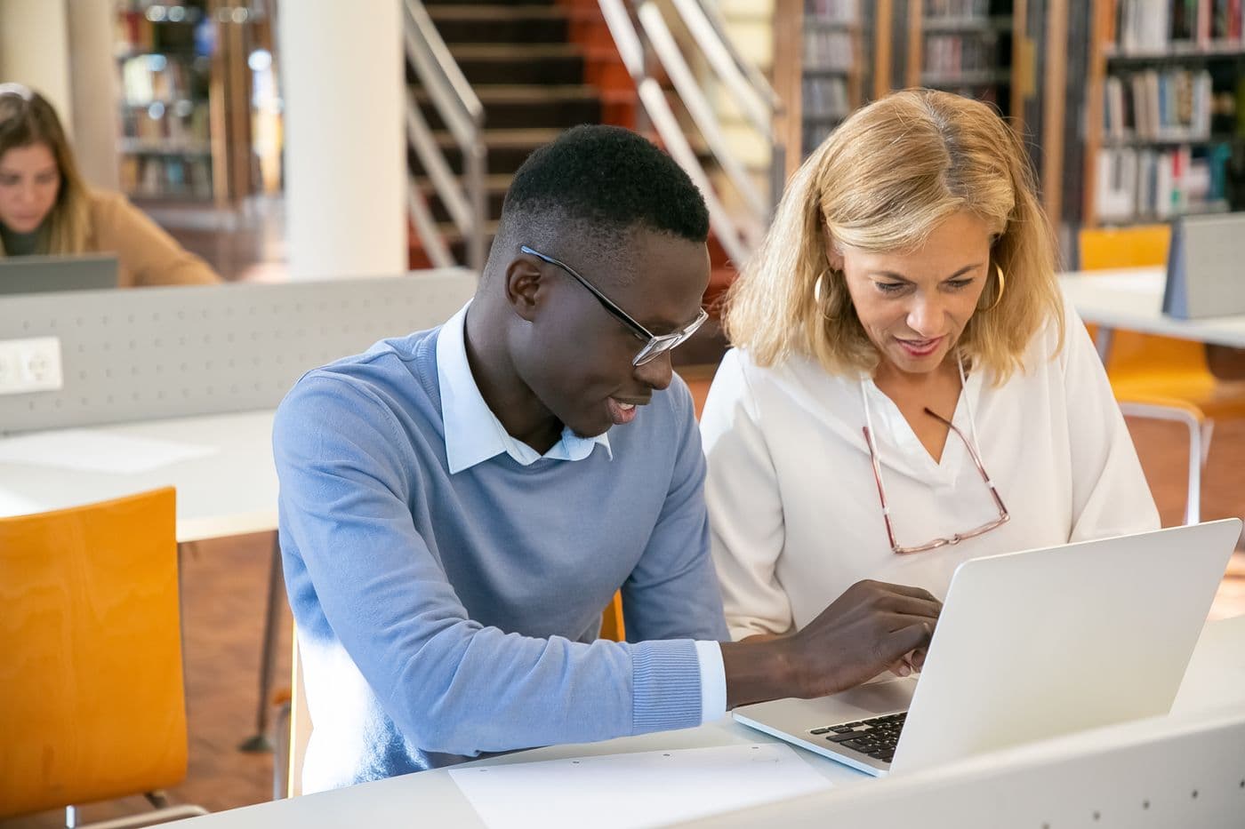 Eine Frau und ein junger Mann arbeiten gemeinsam am Laptop in einer Bibliothek